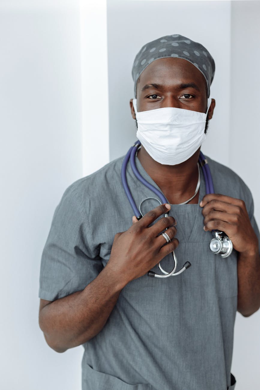 healthcare worker in gray scrubs suit with stethoscope on his neck wearing face mask while looking at the camera